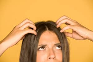 Beautiful young woman with itchy scalp on yellow background